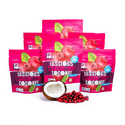 It's Nola Luscious Cranberry Coconut is being placed in a pyramid with a sliced coconut and a cluster of cranberries under the center of the pyramid. The products are placed against a white background.