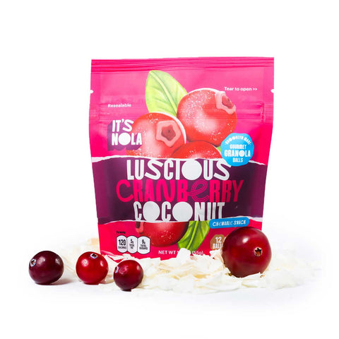 It's Nola Luscious Cranberry Coconut package is surrounded my shredded coconut under the package and cranberries in front of the package.