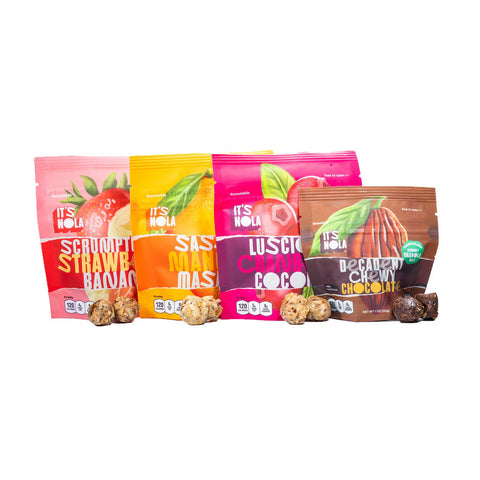 It's Nola Variety Pack is a 4-pack of all of our flavors. They are overlapping each other, and there are two granola bites of each flavor to the bottom right of their corresponding packages. The products are placed against a white background.